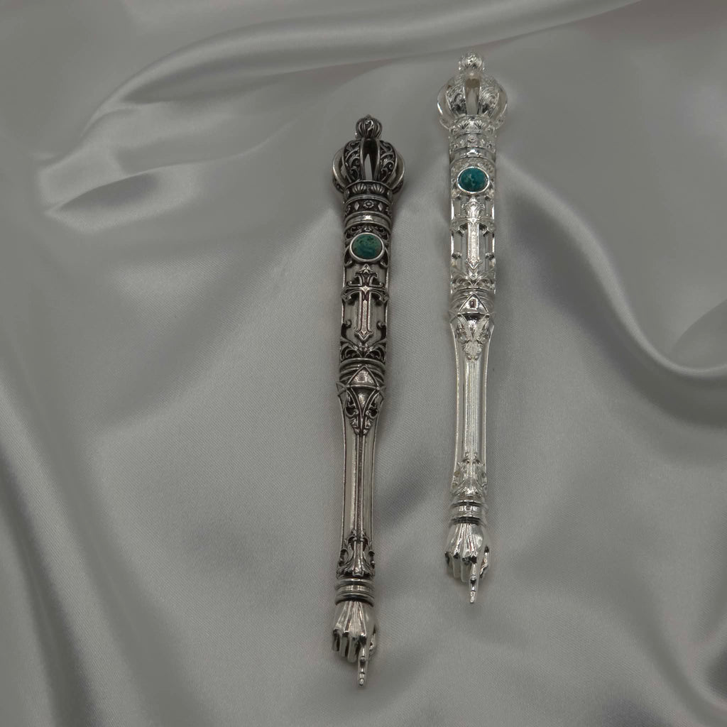 Two samples of the Moriah Cross Works BR-BRSP-001 Bible Reading Pointer displayed side by side on grey silk, showing the antiqued silver finish on the left and the bright mirror-polished silver finish on the right