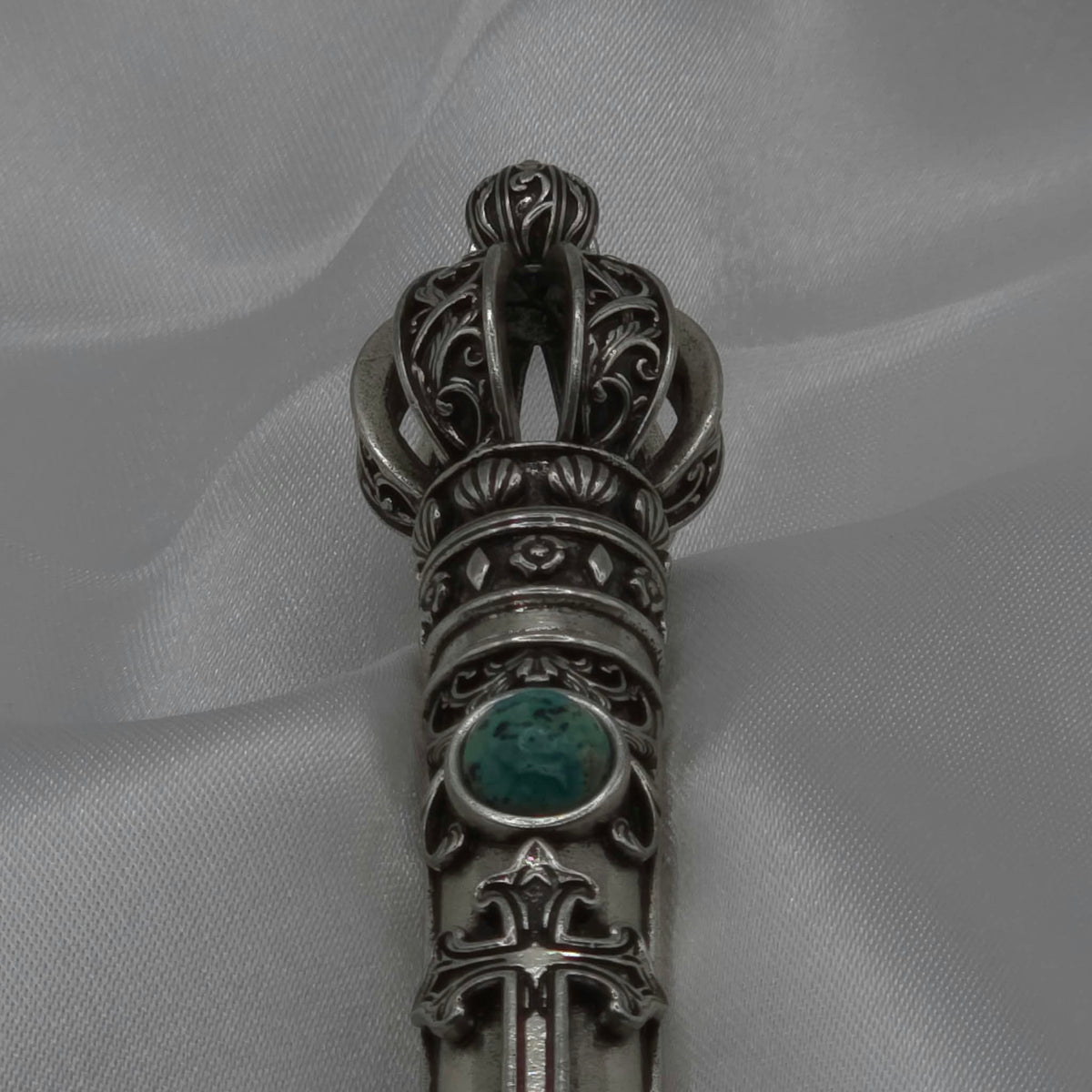 Close-up vertical detail of the filigree crown and upper shaft of the Moriah Cross Works Bible Reading Pointer in antiqued silver, showing deep shadow contrast between the raised ornaments and recessed background, with King Solomon Stone set below the crown
