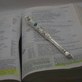 The Moriah Cross Works BR-BRSP-001 Bible Reading silver Pointer sample, resting open on a Bible open to the Psalms, with the King Solomon Stone cabochon visible on the shaft and the ornate pointing hand resting on the scripture text